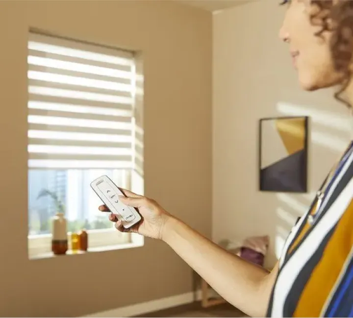 Mulher usando controle remoto para persiana automatizada Somfy